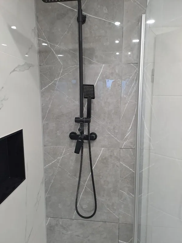 Dusche mit schwarzer Armatur und Fliesen in Marmoroptik